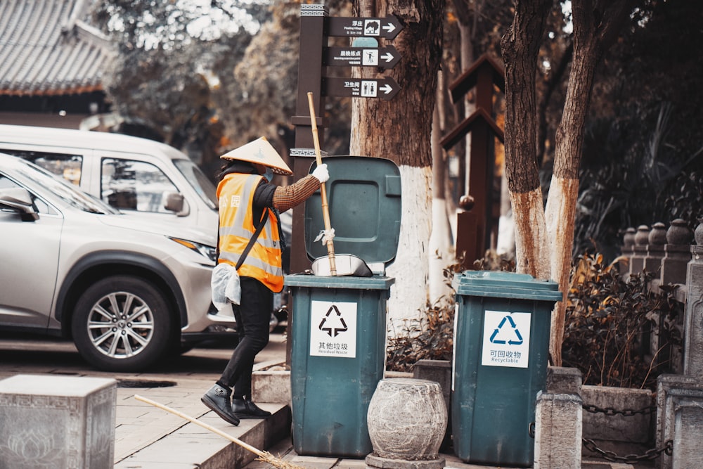 man in yellow jacket and black pants standing beside trash bin