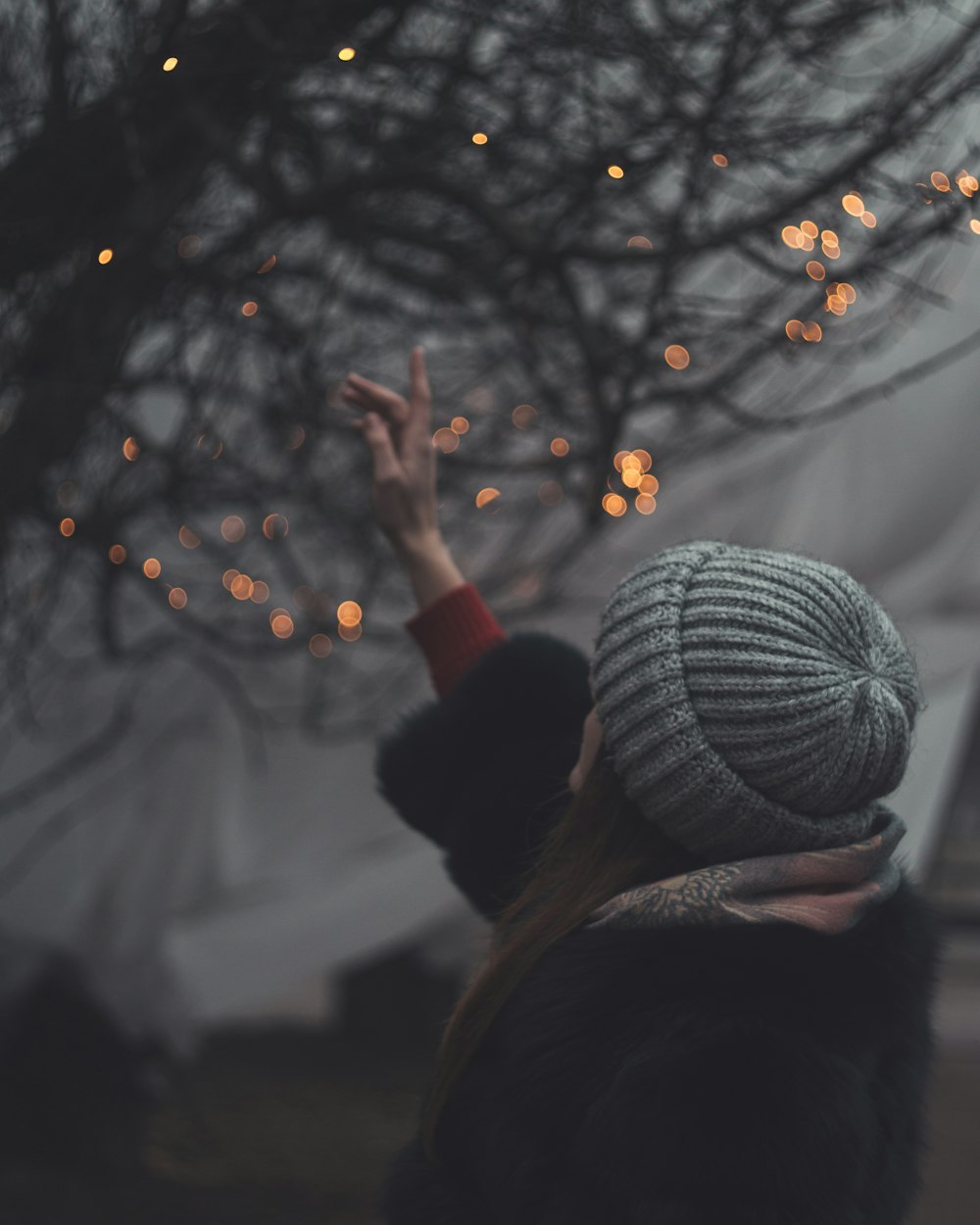 person in black jacket and gray knit cap holding string lights