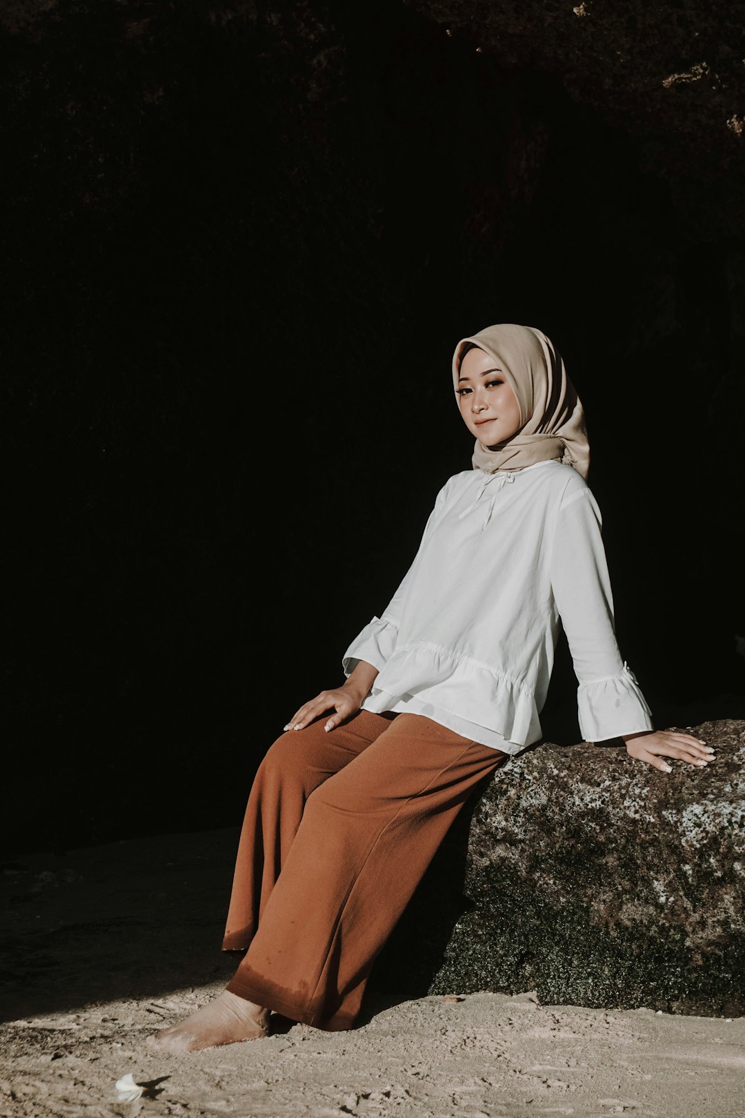 woman in white long sleeve shirt and brown pants sitting on rock