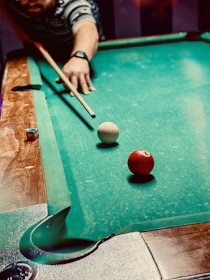 A student practicing shots while watching an online billiards tutorial on a tablet.