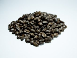 A pile of roasted coffee beans arranged on a light surface, showcasing a glossy texture and rich, dark brown color.