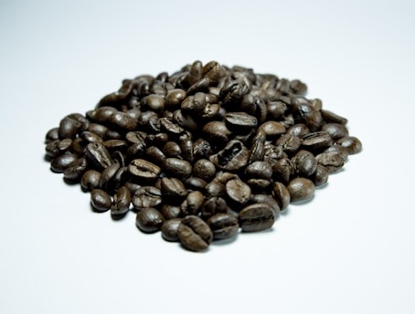 A pile of roasted coffee beans arranged on a light surface, showcasing a glossy texture and rich, dark brown color.