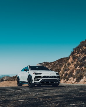A white luxury SUV with tinted windows cruising along a coastal highway.