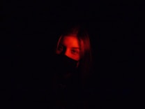 A person is partially illuminated by a red light in an otherwise dark environment, creating a mysterious and dramatic effect.