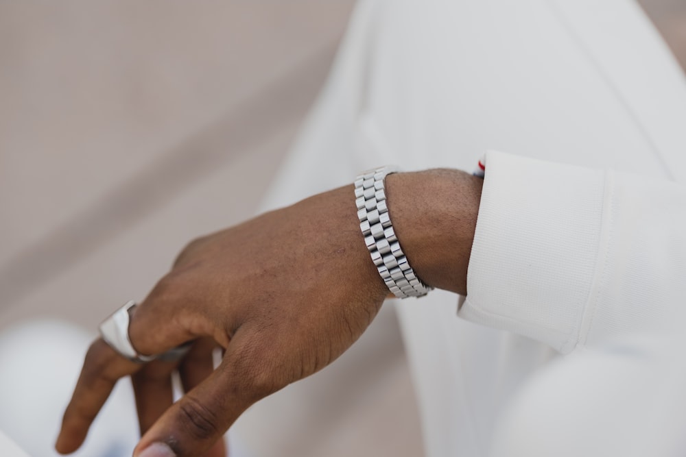 persona che indossa orologio da braccialetto a maglie d'argento