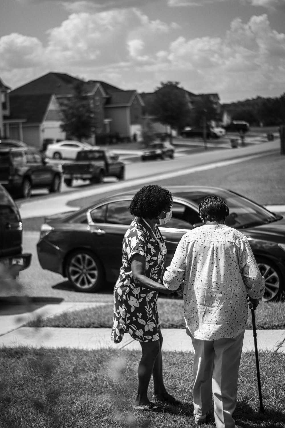 grayscale photo of woman in floral dress standing near car