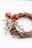 A decorative wreath made of intertwined brown twigs, adorned with green foliage, small red berries, and a dusting of artificial snow, featuring a large red bow.