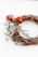 A decorative wreath made of intertwined brown twigs, adorned with green foliage, small red berries, and a dusting of artificial snow, featuring a large red bow.