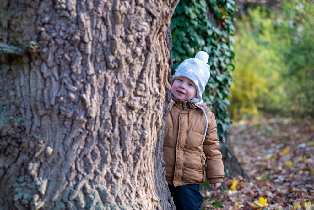 girl in brown jacket standing beside brown tree during daytime