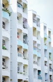 A series of modern apartment balconies arranged in a vertical line, featuring curved designs and different colors on the walls. Some balconies have plants and air conditioning units, and there is clean, minimal architectural detailing.