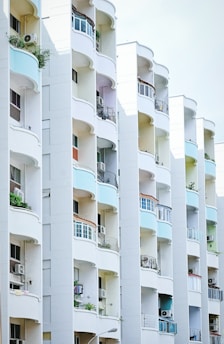 A series of modern apartment balconies arranged in a vertical line, featuring curved designs and different colors on the walls. Some balconies have plants and air conditioning units, and there is clean, minimal architectural detailing.