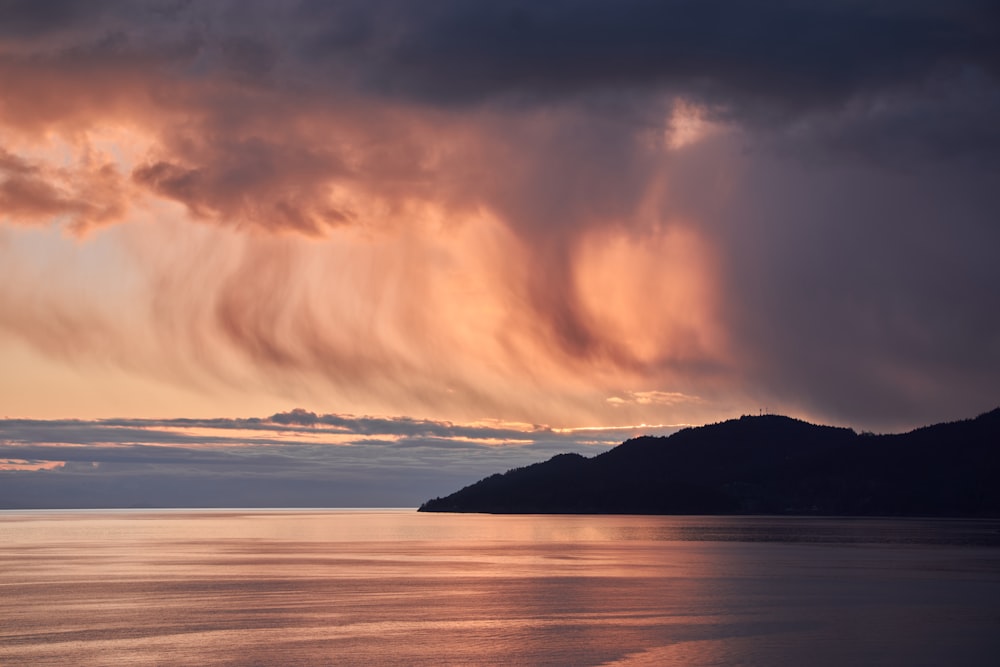 silhouette of mountain near body of water during sunset