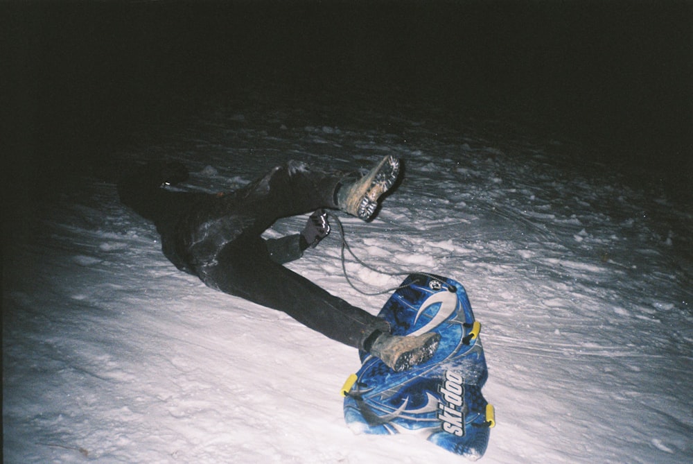 person in black pants and blue shoes sitting on snow covered ground during daytime