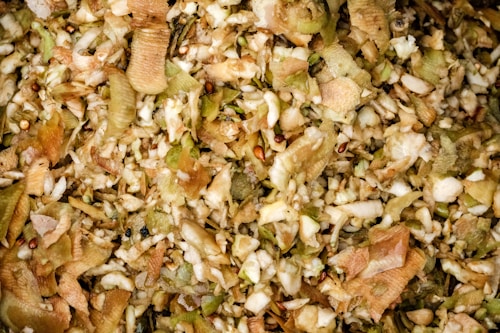 A close-up view of a pile of mixed vegetable and fruit peels, showcasing a variety of textures and colors. The image consists of brown, beige, green, and hints of red peels intermingled, suggesting organic waste or compost material.