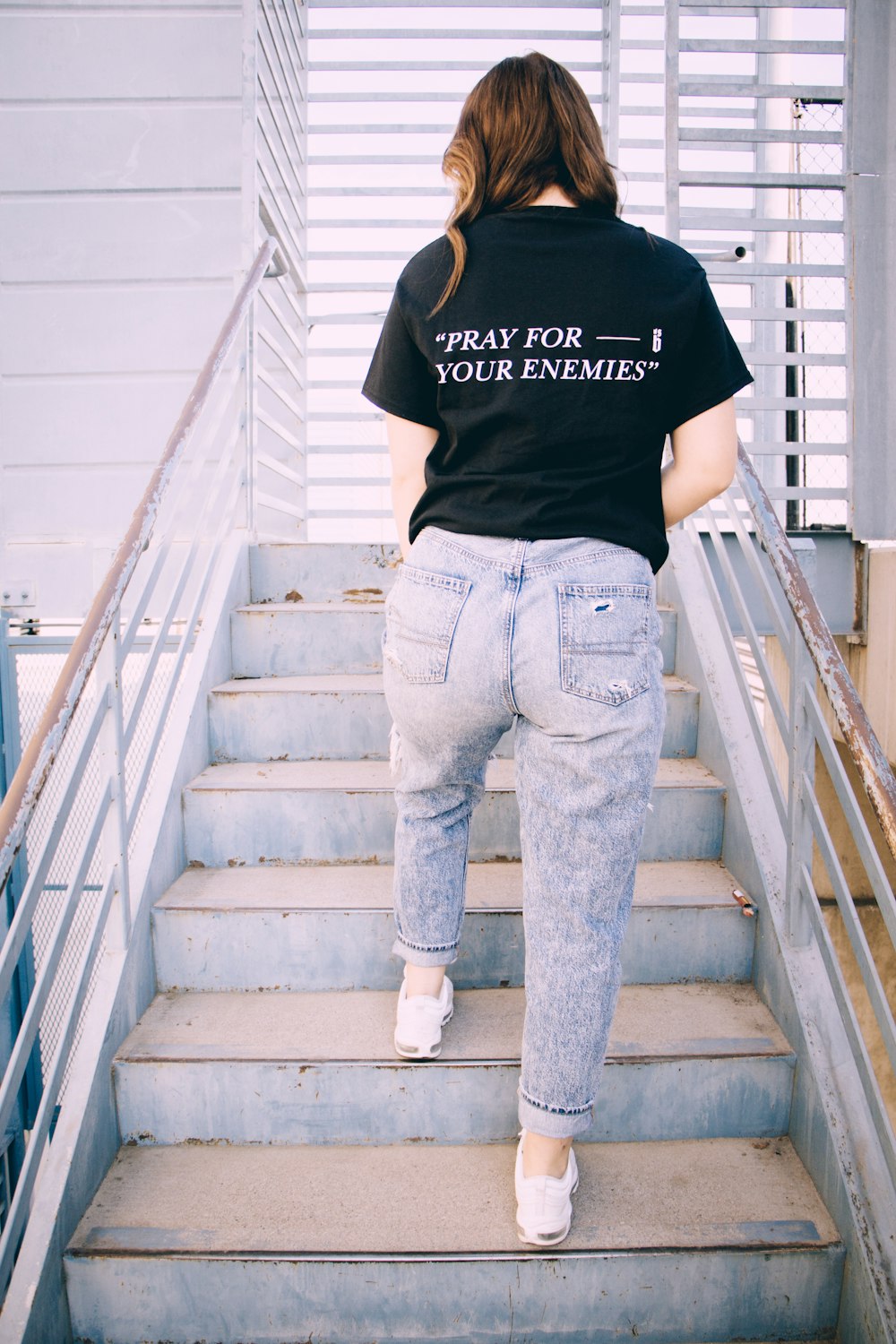 person in black shirt and blue denim jeans standing on gray concrete staircase