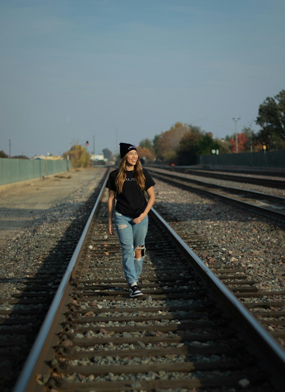 woman in black long sleeve shirt and blue denim jeans standing on train rail during daytime