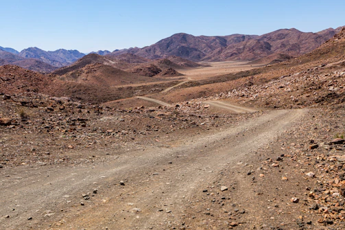 A dirt road winding through open desert land with distant mountains on the horizon.