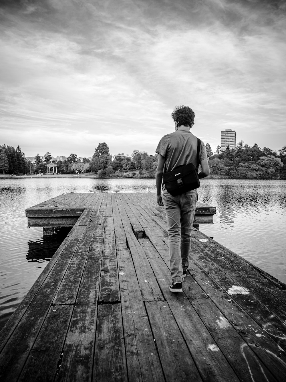man in black jacket and pants standing on wooden dock in grayscale photography