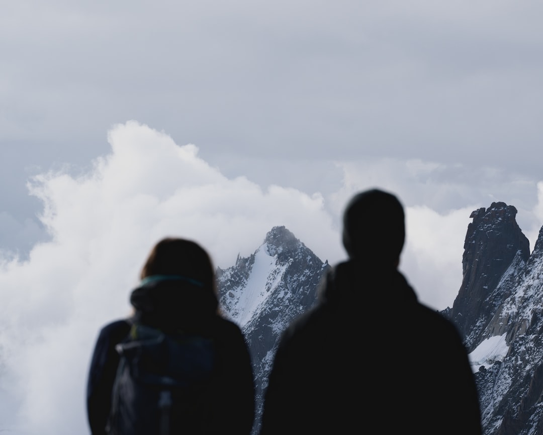 silhouette of 2 person standing on mountain during daytime