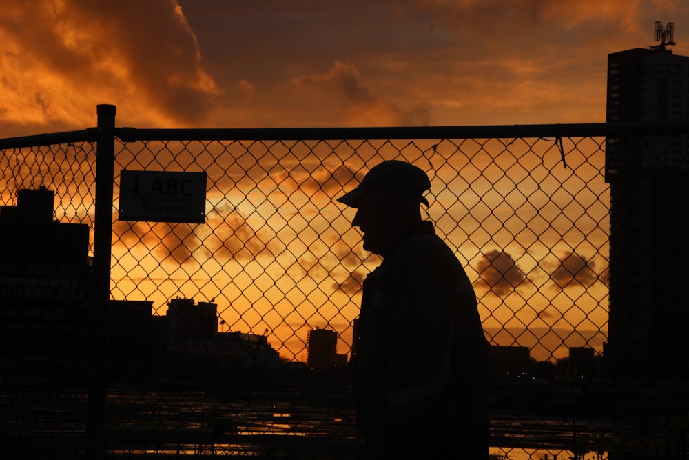 Silueta del hombre de pie cerca de la cerca durante la puesta del sol