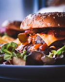 A close-up of a juicy burger featuring a sesame seed bun, melting cheese, and a beef patty, all drizzled with sauce. Fresh lettuce is visible at the base, enhancing the richness of the ingredients.