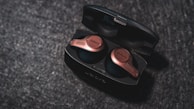 Elegant wireless earbuds in a premium charging case with black and gold finish, displayed on a white marble surface.