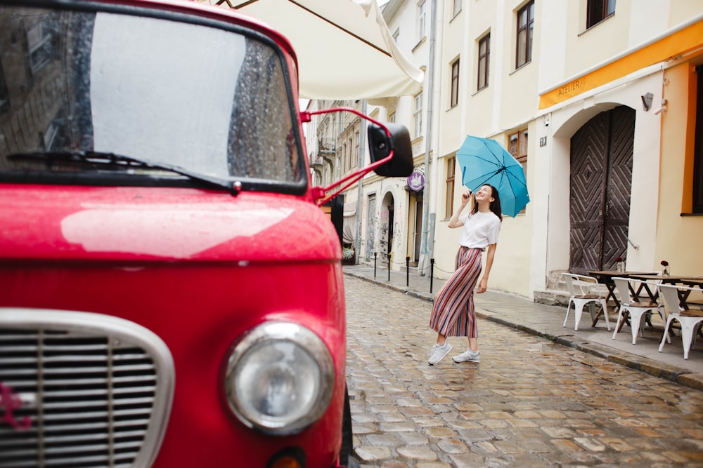 Femme en chemise blanche à manches longues et jupe blanche debout à côté d’une voiture rouge pendant la journée