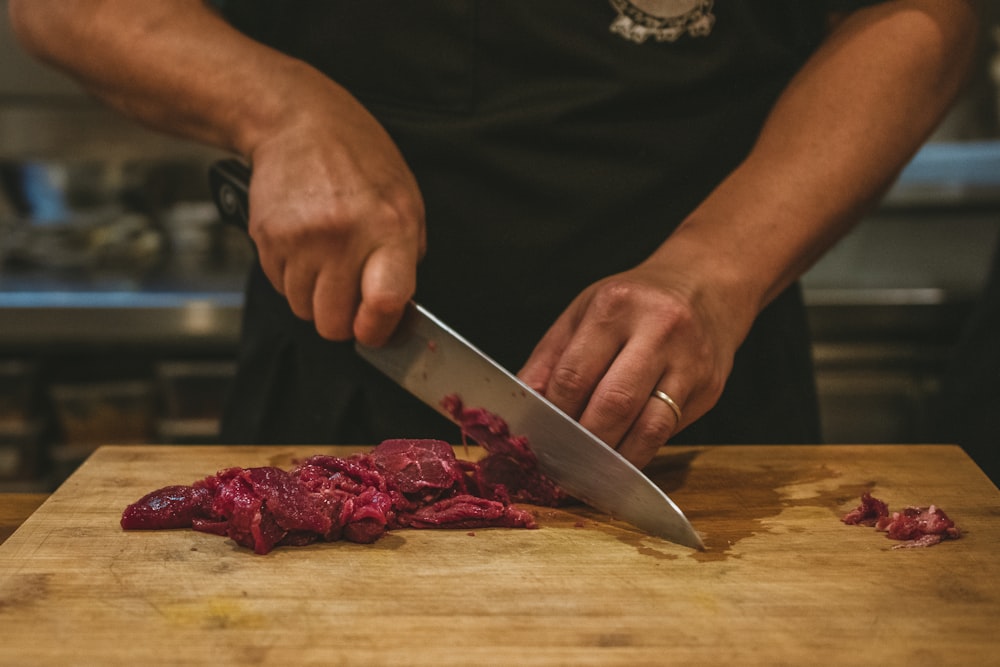 person slicing meat on brown wooden chopping board