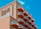 A multi-story hotel building with a distinctive wave-like architectural design. The structure has numerous balconies with white railings, contrasting with the building’s peach-colored exterior. The sky in the background is clear and bright blue. The signage on the building reads 'Paradise Plaza Inn.'