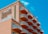 A multi-story hotel building with a distinctive wave-like architectural design. The structure has numerous balconies with white railings, contrasting with the building’s peach-colored exterior. The sky in the background is clear and bright blue. The signage on the building reads 'Paradise Plaza Inn.'