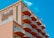 A multi-story hotel building with a distinctive wave-like architectural design. The structure has numerous balconies with white railings, contrasting with the building’s peach-colored exterior. The sky in the background is clear and bright blue. The signage on the building reads 'Paradise Plaza Inn.'