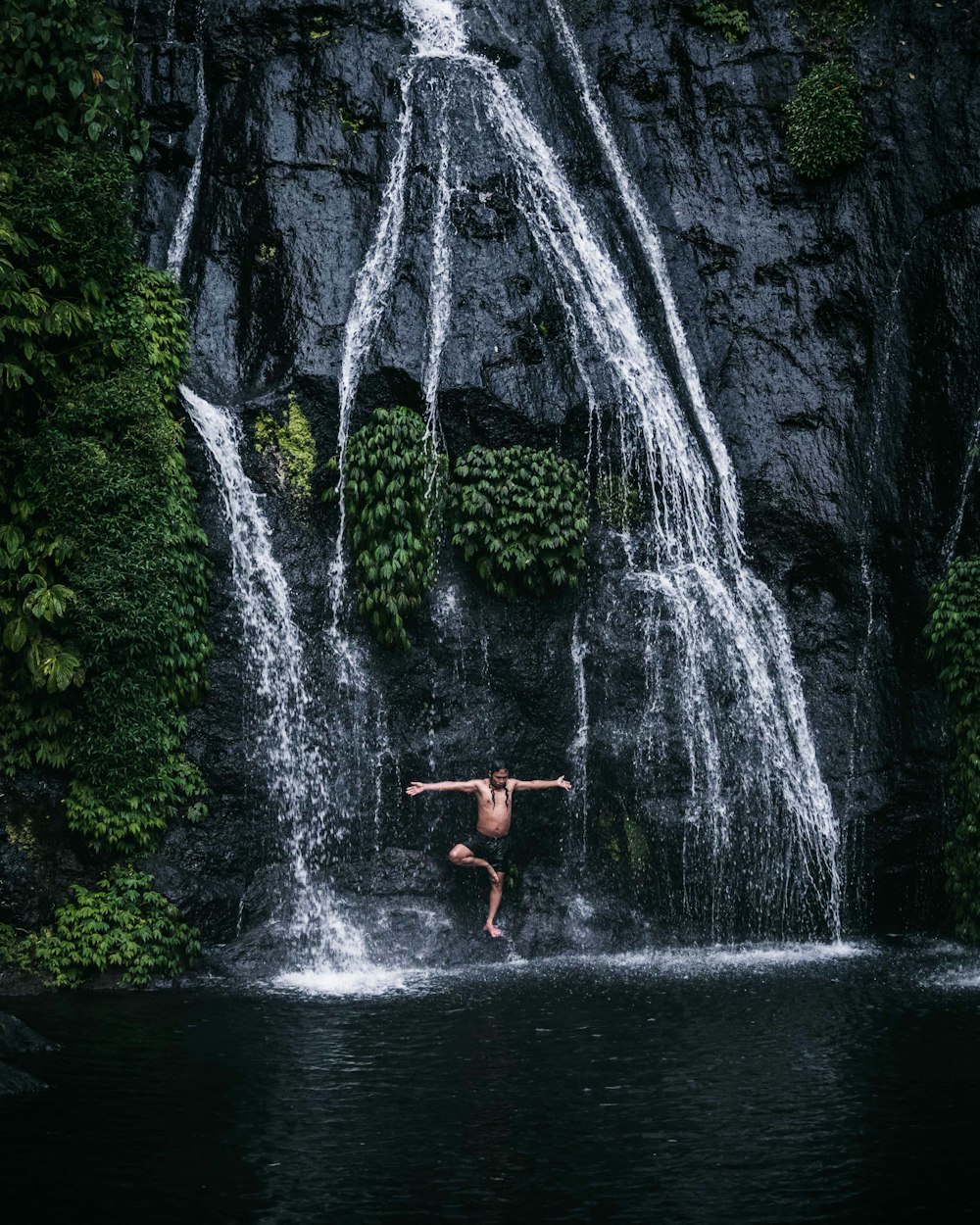 person in red shorts standing on rock in front of waterfalls during daytime