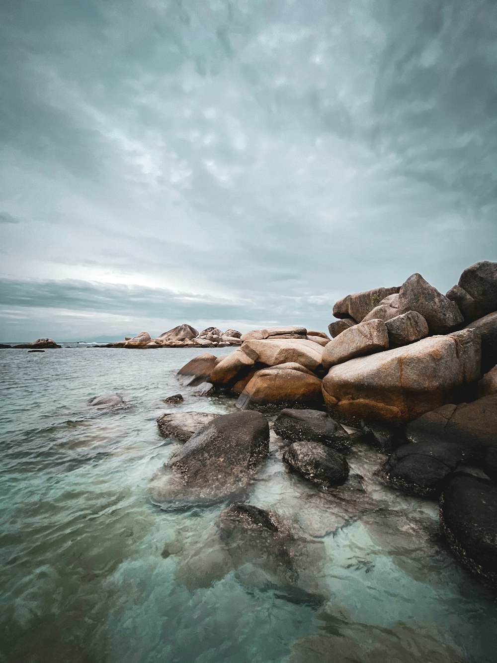 brown rocks on sea under white clouds and blue sky during daytime