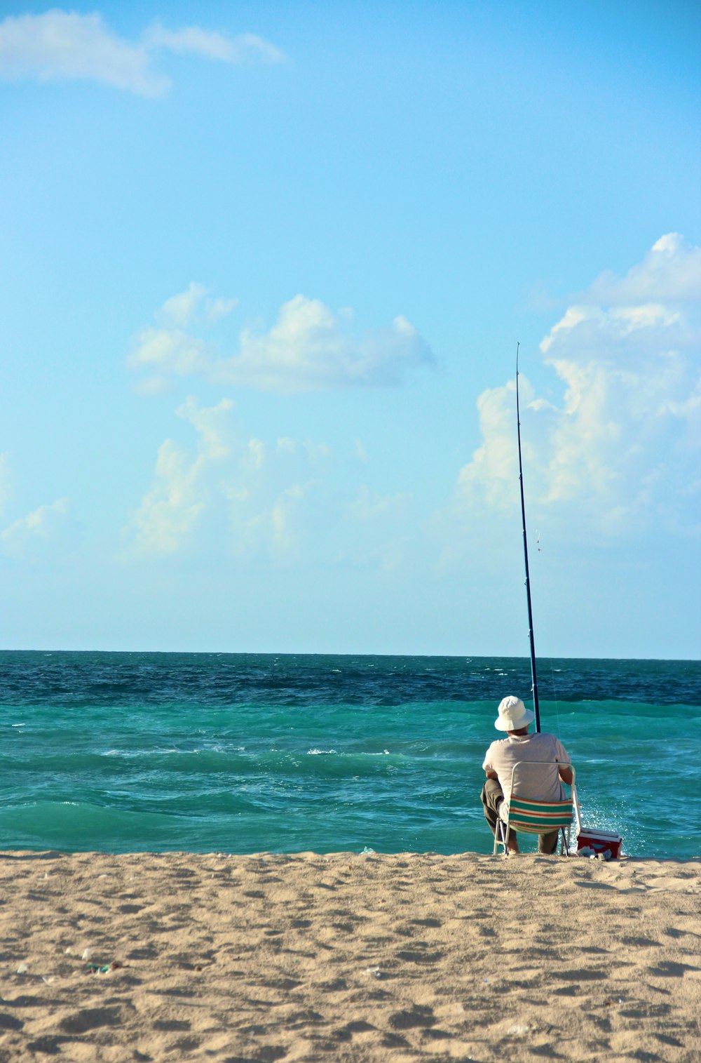 Uomo in maglietta bianca che si siede sulla panchina di legno marrone sulla spiaggia durante il giorno