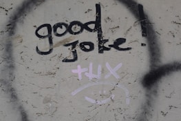 Graffiti on a textured wall displays the words 'good joke!' in bold black paint. Below it, the word 'thx' and a smiley face are drawn in light pink.