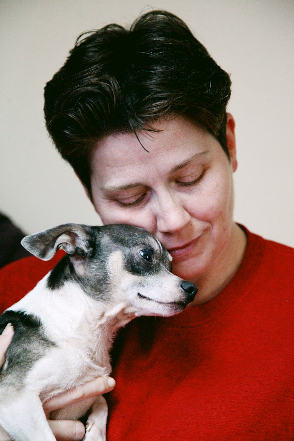 woman in red shirt holding white and black short coat small dog