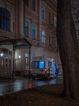 Paramedics assisting a patient into a rapid-response ambulance at dusk near a hospital entrance.