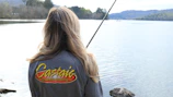 A seasoned fishing influencer casting a line by a sparkling lake at dawn, gear branded with bluecurrent partnership