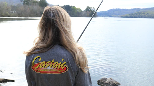 A seasoned fishing influencer casting a line by a sparkling lake at dawn, gear branded with bluecurrent partnership