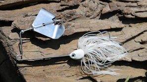 Close-up of a handcrafted bottle cap fishing lure resting on weathered wood.