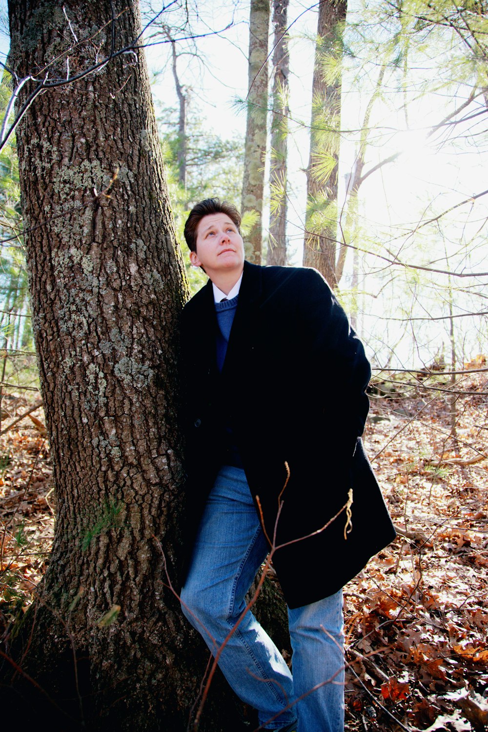 hombre con abrigo negro y jeans de mezclilla azul sentado en un árbol