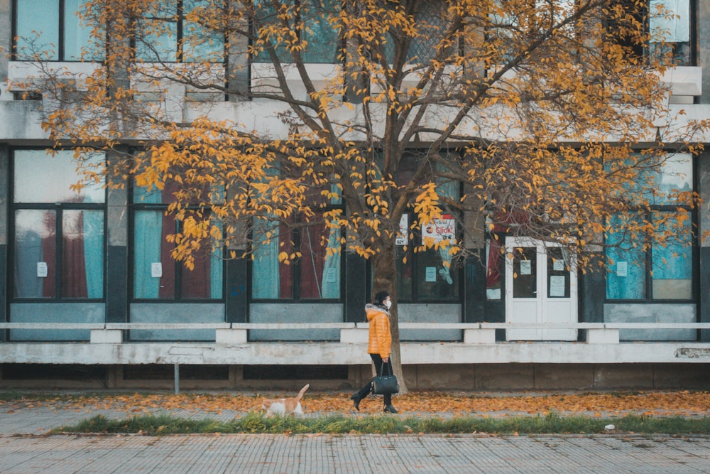 woman in black jacket and black pants standing on sidewalk near blue building during daytime