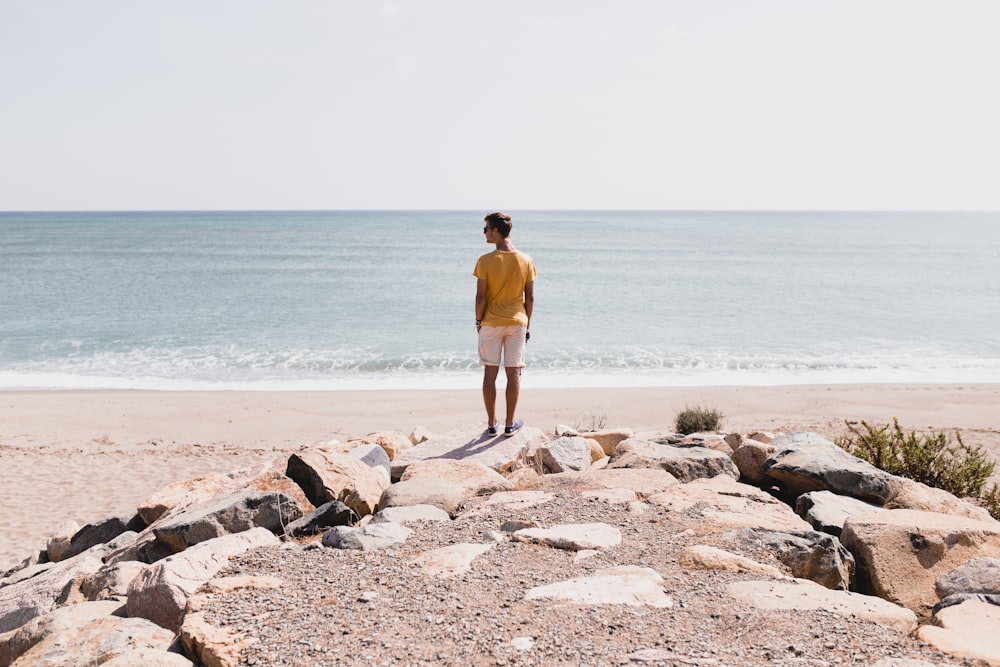 woman in brown shorts standing on rocky shore during daytime