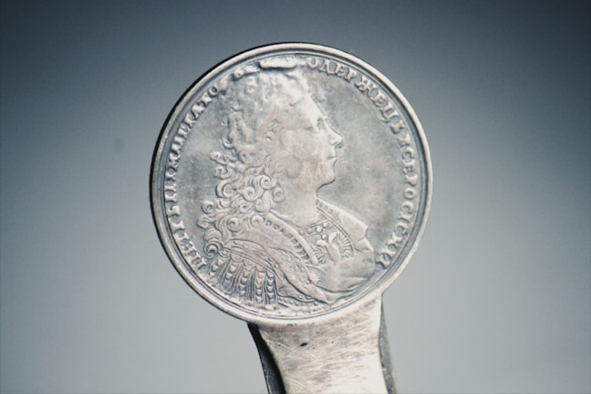 An antique silver coin held gently between two fingers.