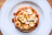 A stack of mini hotcakes topped with sliced bananas, walnuts, and a light dusting of powdered sugar on a pastel plate.