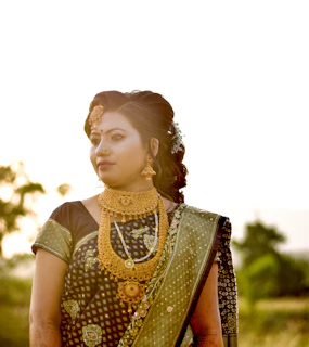 A serene portrait of a woman wearing a maroon saree with gold borders, standing beside a traditional Indian jharokha window.