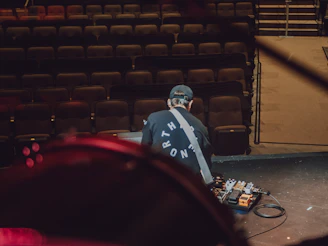 Technician adjusting guitar equipment on stage with focused lighting.