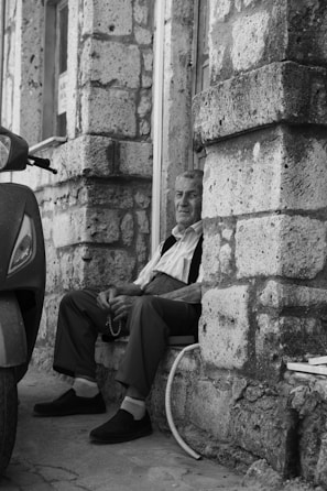 An elderly man sitting contemplatively on a worn bench in a narrow alley of Bangkok.