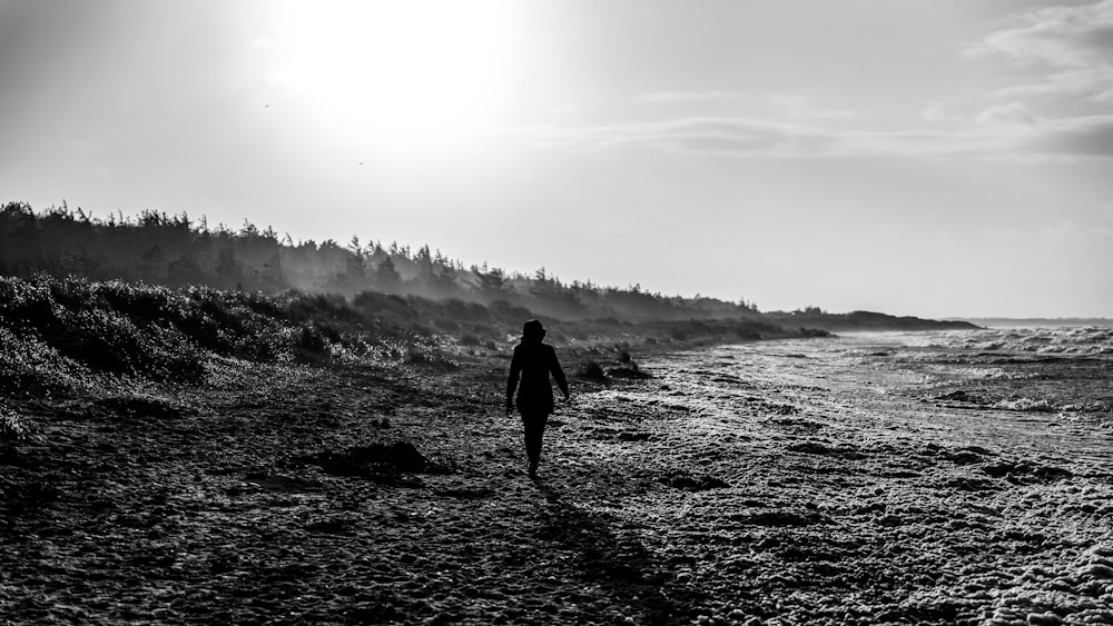 grayscale photo of man walking on beach