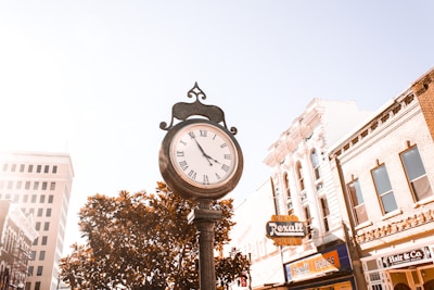 A charming street clock illuminating a quaint downtown street lined with shops in the evening.
